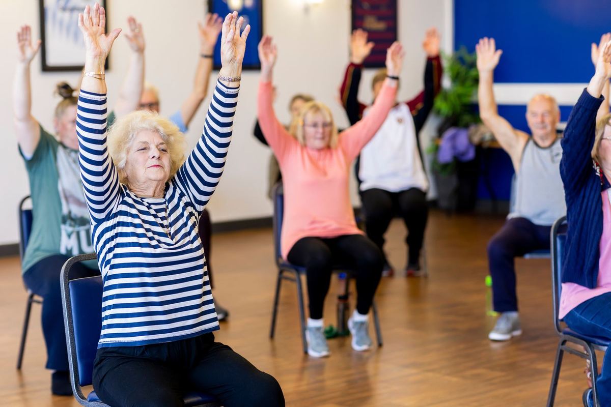 A group of older adults, men and women, taking part in a seated exercise class